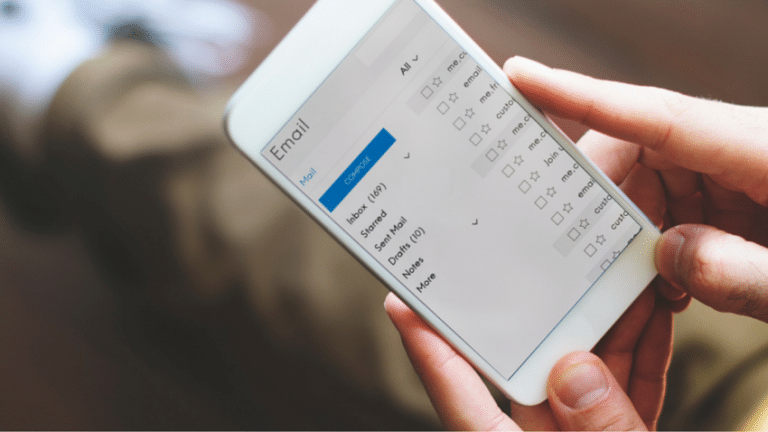 A person holds a smartphone displaying an email interface with folders labeled 'Inbox', 'Sent Mail', 'Drafts', and options for sorting.