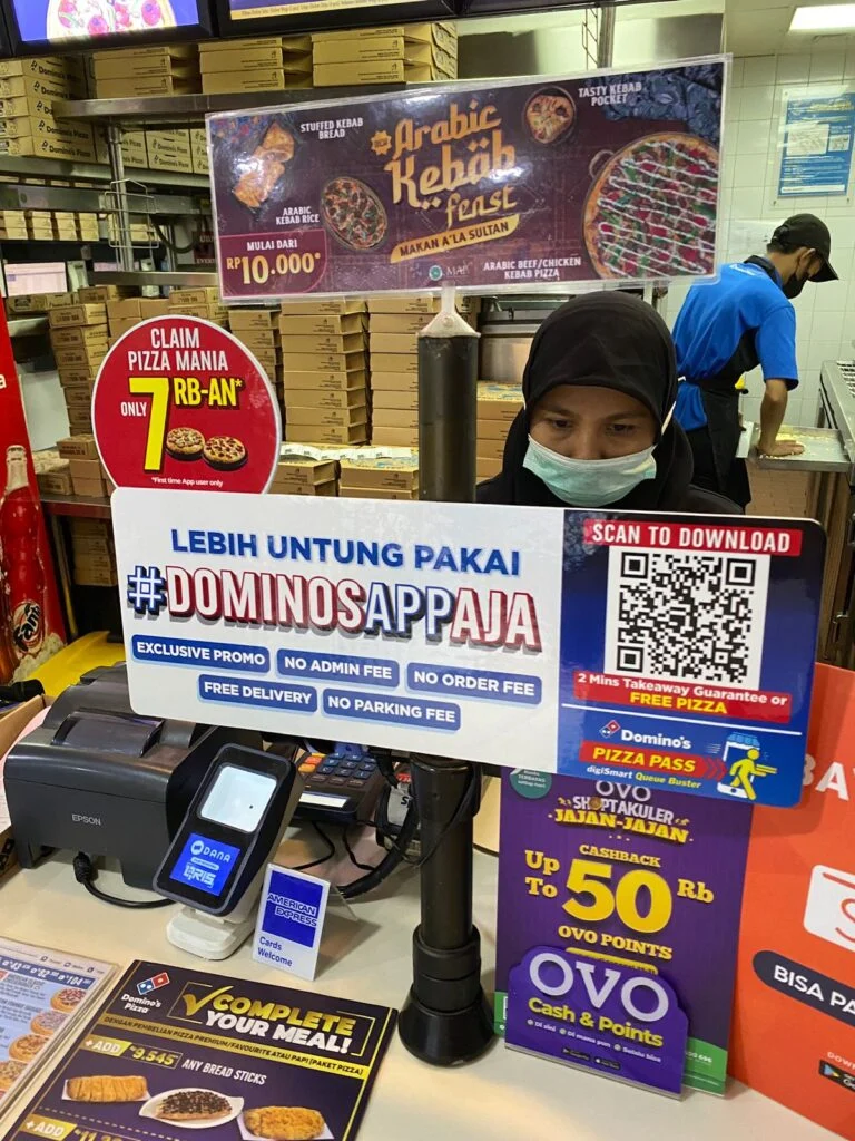 Photo of a dominos store in Indonesia with a QR code to scan at the counter
